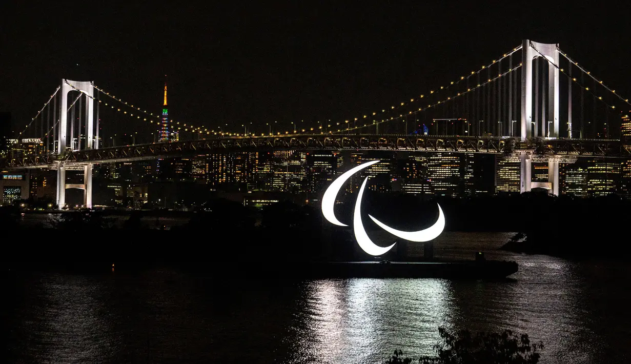 Simbol Paralimpiade menyala pada malam hari dengan latar belakang Jembatan Pelangi dan Menara Tokyo di tepi Pantai Odaiba, Tokyo, Jepang, 23 Agustus 2021. Paralimpiade Tokyo 2020 mulai 24 Agustus 2021 sampai 5 September 2021. (Charly TRIBALLEAU/AFP)