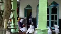 Para siswa SD Negeri Pelangwot mengerjakan soal ujian sambil duduk di lantai.