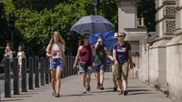 Turis memegang payung untuk berlindung dari matahari, di London, Senin (18/7/2022). Pemerintah Inggris telah mengeluarkan peringatan suhu panas ekstrem pertama di negara itu, sementara cuaca panas dan kering yang telah melanda daratan Eropa selama seminggu terakhir bergerak ke utara, mengacaukan perjalanan, layanan kesehatan, dan sekolah. (AP Photo/Alberto Pezzali)