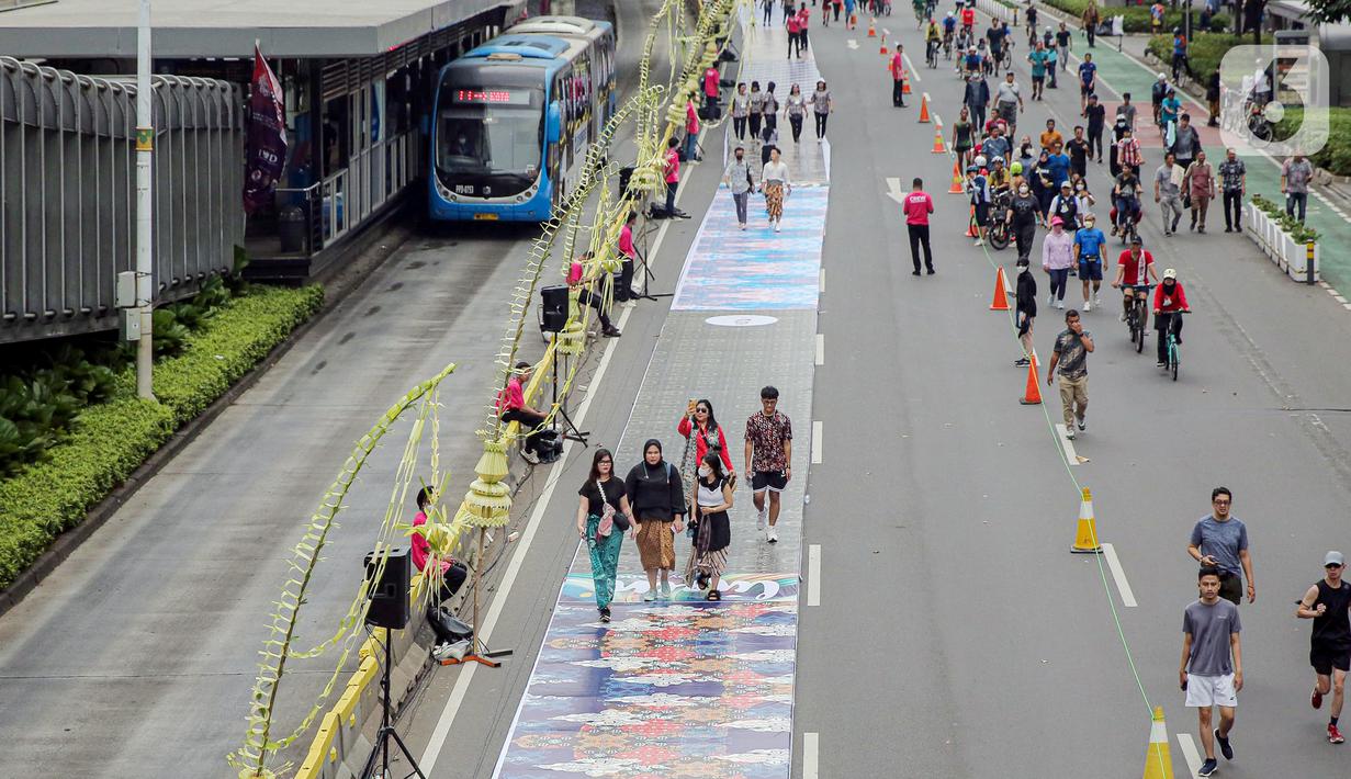 Sejumlah orang yang mengenakan batik berjalan di catwalk sepanjang Jalan Jenderal Sudirman, Jakarta, Minggu (2/10/2022). Kegiatan yang diikuti ratusan orang ini diselenggarakan oleh Bank Mandiri untuk menyambut Hari Batik Nasional yang jatuh setiap tanggal 2 Oktober 2022. (Liputan6.com/Faizal Fanani)
