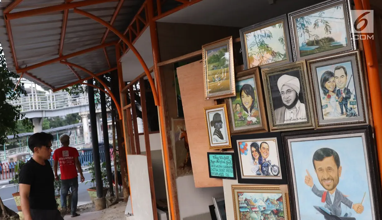 Seniman lukis memasang lukisan pada dinding yang berada di Sentra Lukisan Pasar Baru, Jakarta, Jumat (16/11). Sejumlah seniman lukis mengeluhkan kondisi lapak Sentra Lukisan Pasar Baru. (Liputan6.com/Immanuel Antonius)