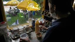 Foto yang diambil 31 Mei 2021 menunjukkan seorang pekerja membuat kopi di gerbong kereta yang diubah menjadi kafe di stasiun kereta api di Phnom Penh. Gerbong kereta diubah menjadi kafe setelah selama pandemi corona sebagian besar perjalanan kereta api di Kamboja dihentikan. (TANG CHHIN Sothy/AFP)