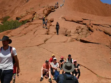 Wisatawan mendaki Uluru yang juga dikenal sebagai Batu Ayers di Taman Nasional Uluru-Kata Tjuta, utara Australia, Jumat (25/10/2019). Kawasan wisata bukit batu Uluru dipenuhi pengunjung, lantaran hari ini merupakan hari terakhir sebelum larangan pendakian diberlakukan. (SAEED KHAN / AFP)
