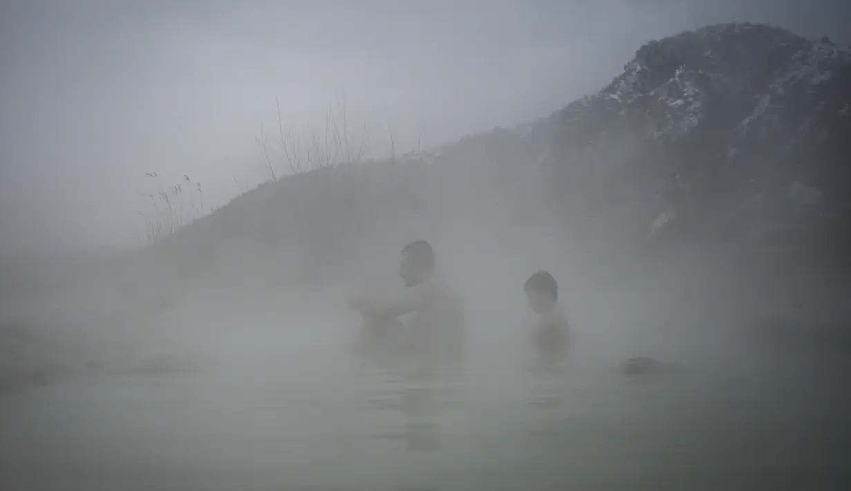 Orang-orang menikmati air panas di mata air mineral alami pada hari musim dingin di dekat desa Rupite, Bulgaria (2/2/2022). Penduduk setempat percaya bahwa air mineral menyembuhkan banyak penyakit dan gangguan. (AFP/Nikolay Doychinov)