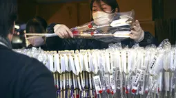 Seorang staf menjual Hamaya, atau panah ritual, untuk mengusir roh jahat di kuil Kawasaki Daishi, di mana banyak pengunjung berdoa untuk keberuntungan selama "hatsumode" atau kunjungan pertama tahun ini ke kuil atau kuil, di Kawasaki, dekat Tokyo , Senin, 2 Januari 2023. (AP Photo/Eugene Hoshiko)