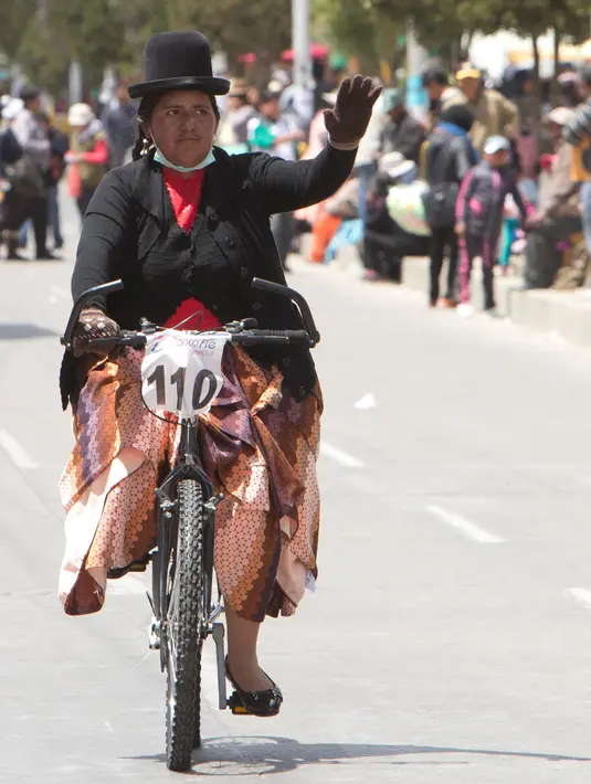 Seorang wanita melambaikan tangan saat mengikuti balapan sepeda Cholita di El Alto, La Paz, Bolivia (12/11). Pemenang dalam balapan ini berhak membawa pulang sepeda. (AP Photo / Juan Karita)