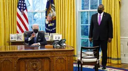 Menteri Pertahanan Lloyd Austin mendengarkan Presiden AS Joe Biden berbicara sebelum menandatangani Perintah Eksekutif yang membatalkan larangan bagi transgender untuk masuk militer AS pada era Donald Trump di Kantor Oval Gedung Putih, Washington, Senin (25/1/2021). (AP Photo/Evan Vucci)