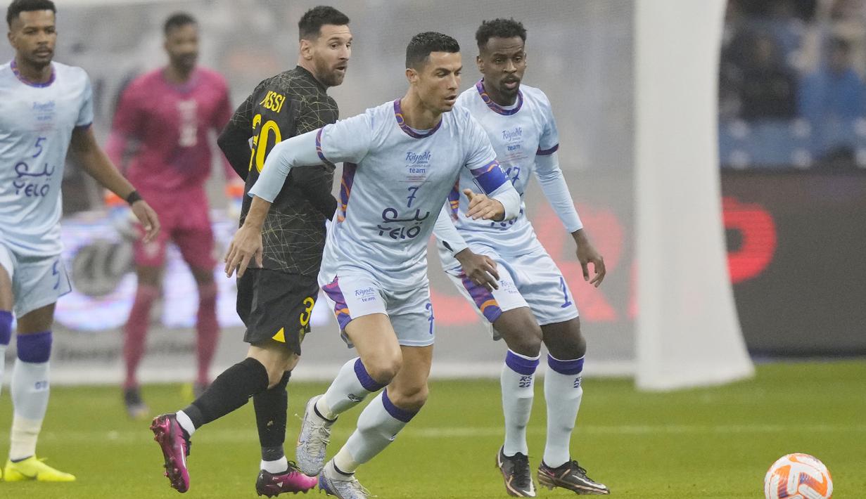 Pemain Paris Saint-Germain (PSG), Lionel Messi melihat pemain Riyadh All-Star, Cristiano Ronaldo, menggiring bola pada laga persahabatan di Stadion Raja Fahd pada Jumat (20/1/2023). Hujan gol mewarnai laga ini. PSG menang dengan skor ketat 5-4. (AP Photo/Hussein Malla)
