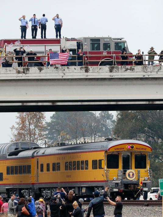 Petugas pemadam kebakaran dan warga memberi hormat saat kereta pembawa peti jenazah Presiden ke-41 AS George HW Bush melintasi Spring, Texas, Kamis (6/12). Bush akan dimakamkan di Museum Perpustakaan Kepresidenan George HW Bush. (AP Photo/Michael Wyke)