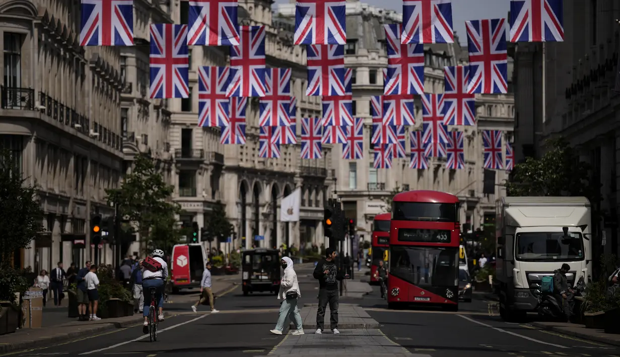 <p>Orang-orang melintasi distrik perbelanjaan Regent Street dengan bendera Union tergantung menandai Platinum Jubilee untuk 70 tahun kepemimpinan Ratu Elizabeth II, di London, Rabu (18/5/2022). Tingkat inflasi Inggris naik ke level tertinggi dalam 40 tahun pada bulan April karena invasi Rusia ke Ukraina memicu kenaikan lebih lanjut dalam harga makanan dan bahan bakar. (AP Photo/Matt Dunham)</p>