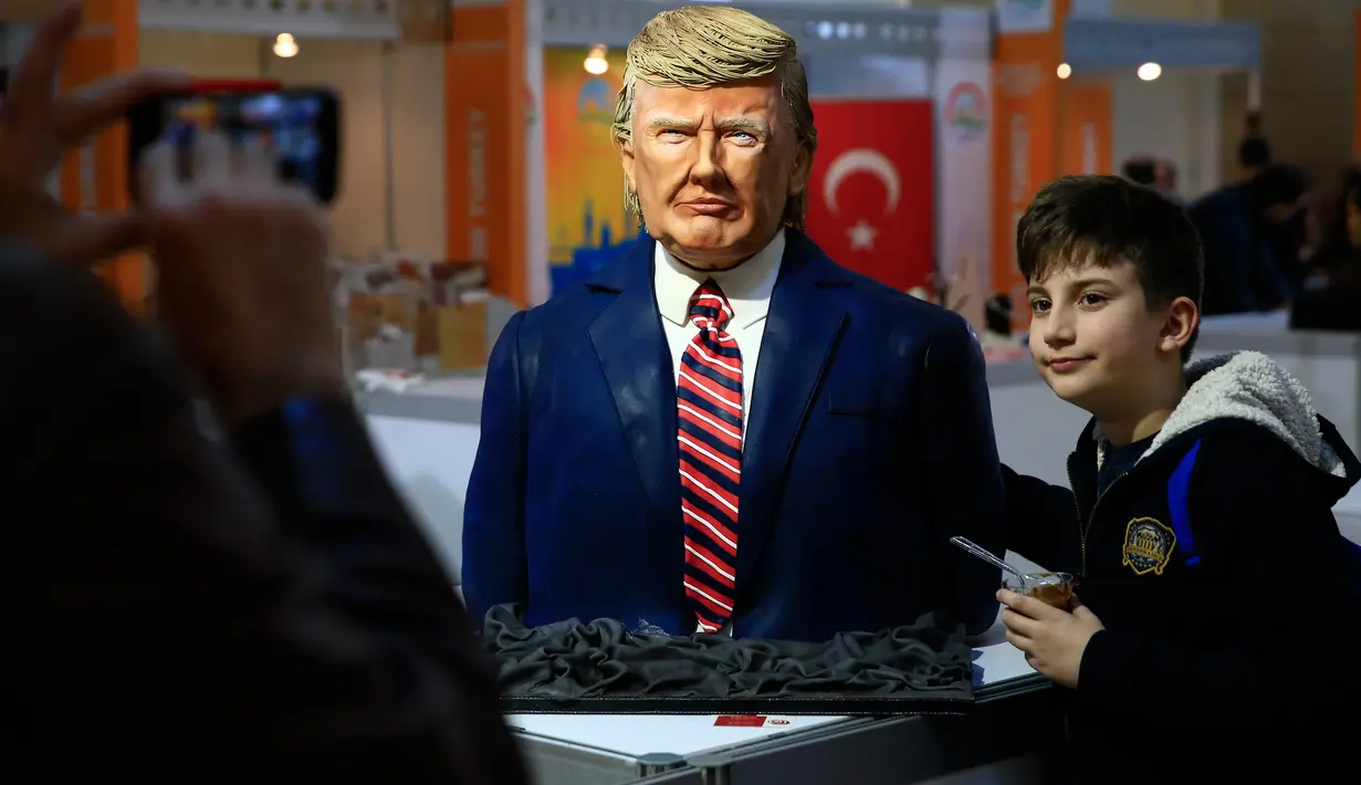 Seorang anak berpose dengan patung Presiden AS Donald Trump yang terbuat dari cokelat dalam Festival Cokelat Turki di museum militer Istanbul, 25 Maret 2017.Karya seni lezat itu dibuat oleh chef perempuan Turki, Tuba Geckil. (AP Photo/Lefteris Pitarakis)
