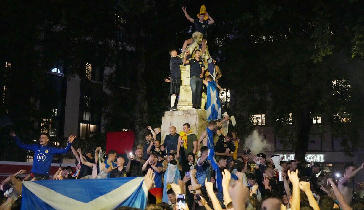 Suporter Skotlandia berkumpul dan merayakan keberhasilan negaranya menahan imbang Inggris pada laga Euro 2020 di patung William Shakespeare di Leicester Square, London, Jumat (18/6/2021). (AP/Kirsty Wigglesworth)