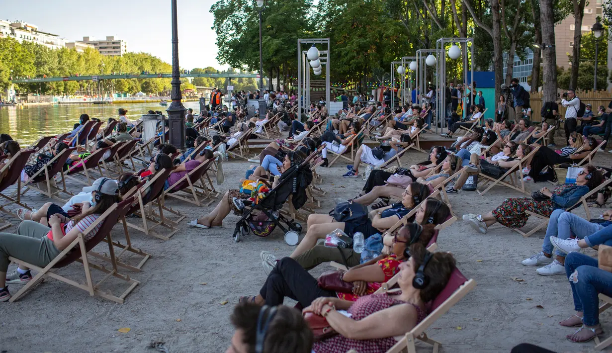Orang-orang menghadiri Cinema on the Water, yang diselenggarakan Paris Plages selama pemutaran "Le Grand Bain" di Paris, Prancis pada 18 Juli 2020. Paris menghadirkan terobosan baru dengan bioskop terapung lengkap dengan perahu yang tetap menjaga jarak. (AP Photo/Rafael Yaghobzadeh)