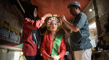Seorang perempuan dengan pakaian tradisional dibantu menyiapkan hiasan bunga di rambutnya untuk berpartisipasi dalam Festival Ngarot di Lelea, Indramayu , Jawa Barat, pada 13 Desember 2023. (Timur MATAHARI/AFP)