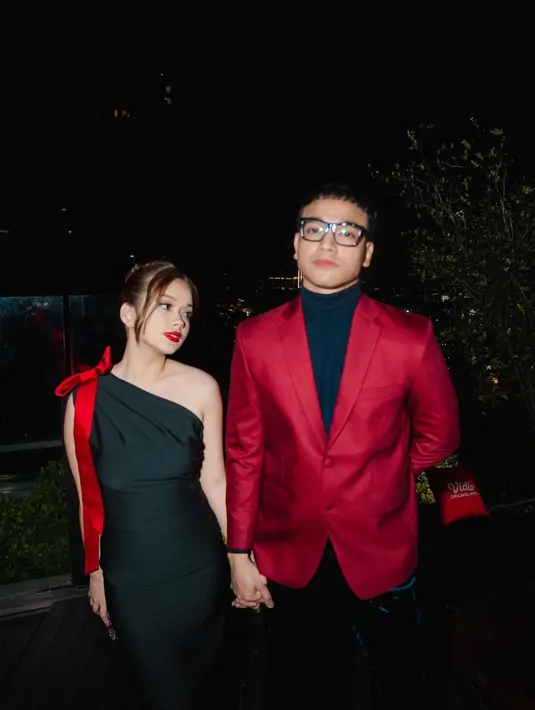 <p>Tampilan Fadly dan Rebecca kali ini bisa jadi inspirasi gaya dinner romantis. Fadly dengan blazer merah dengan innerwear turtleneck biru navy, sedangkan Rebecca tampil dengan dress hitam asimetris berwarna hitam berdetail pita merah menambah kesan sensual pada tampilannya yang sudah sempurna. Foto: Instagram.</p>