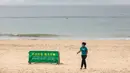Seorang wanita berjalan melewati papan petunjuk saat para pekerja mulai menutup Pantai Shek O di Hong Kong, Kamis (17/3/2022). Pemerintah Hong Kong mengatakan akan menutup pantai umum untuk mengekang penyebaran virus corona COVID-19. (DALE DE LA REY/AFP)