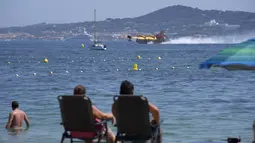 Wisatawan menyaksikan pesawat pelempar air mengisi tangkinya di pantai di Sainte-Maxime, Prancis selatan, Rabu (18/8/2021). Lebih dari 1.100 petugas pemadam kebakaran berjuang melawan api dan ribuan turis dan penduduk lokal dievakuasi ke daerah yang lebih aman. (AP Photo/Daniel Cole)