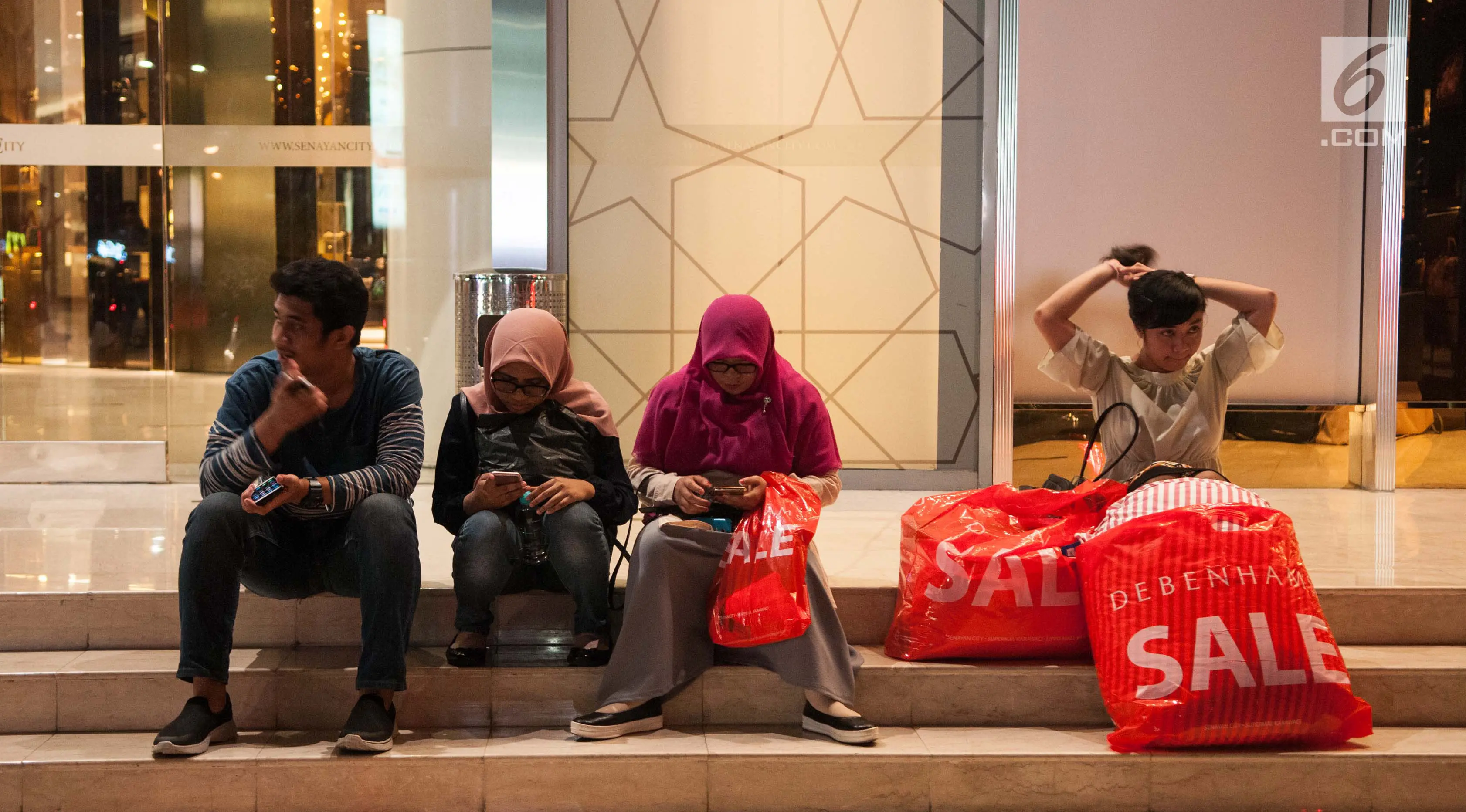 Sejumlah orang menunggu kendaraan sambil membawa barang belanjaannya usai mengunjungi Midnight Sale" di Mall Senayan City, Jakarta, Jumat (16/6). (Liputan6.com/Gempur M Surya)