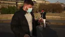 Seorang pria berjalan dengan masker untuk mencegah penyebaran virus corona COVID-19, saat seorang pria mengambil foto matahari terbenam, di Paris (29/3/2021). (AP Photo/Thibault Camus)