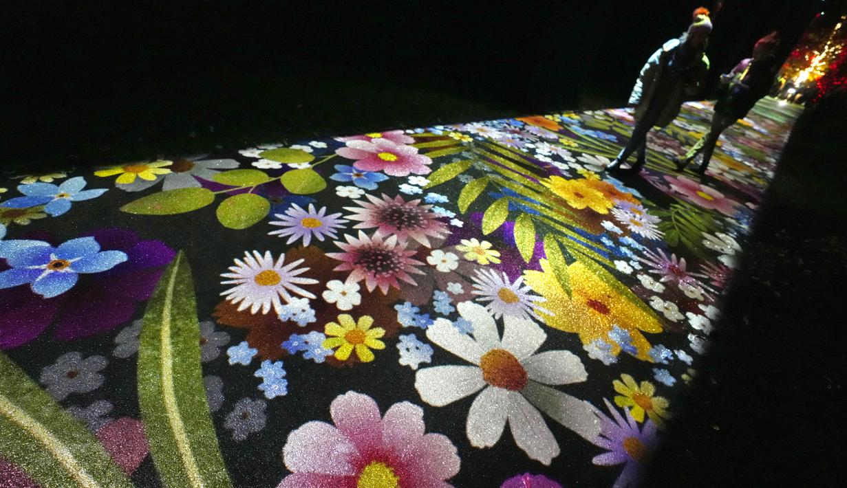 Orang-orang berjalan di sepanjang jalan yang menampilkan imersif dengan visual bunga-bunga, bagian dari instalasi cahaya yang dipamerkan menyambut Natal di Royal Botanic Gardens, Kew, London, Selasa (15/11/2022). Selain memamerkan jalur cahaya dengan satu juta lampu di jalur sepanjang 2,7 km, terdapat cahaya imersif, pohon lampu, terowongan cahaya, dan pertunjukkan cahaya air yang mengesankan. (AP Photo/Kirsty Wigglesworth)