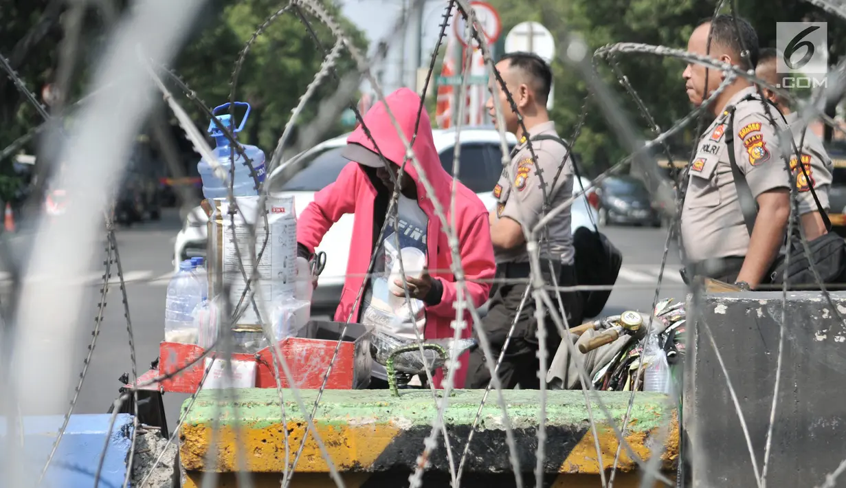 Seorang pedagang terlihat di dekat kawat berduri yang memblokade jalan ke arah gedung KPU, Jakarta Pusat, Minggu (30/6/2019). Penjagaan gedung KPU diperketat menjelang rapat pleno terbuka penetapan pasangan calon presiden dan wakil presiden terpilih Pemilu 2019. (merdeka.com/Iqbal S Nugroho)