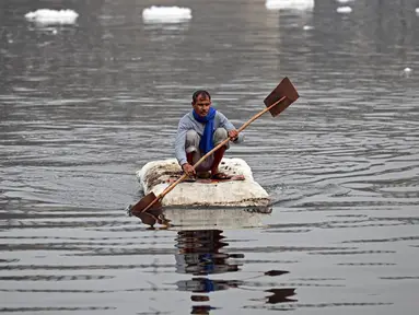 Seorang pria mendayung rakitnya sambil mengumpulkan bahan-bahan daur ulang dekat potongan busa tercemar yang mengambang di Sungai Yamuna, New Delhi, India, 26 Desember 2021. Lapisan busa beracun melapisi sungai yang dianggap suci oleh umat Hindu, Sungai Yamuna. (Sajjad HUSSAIN/AFP)