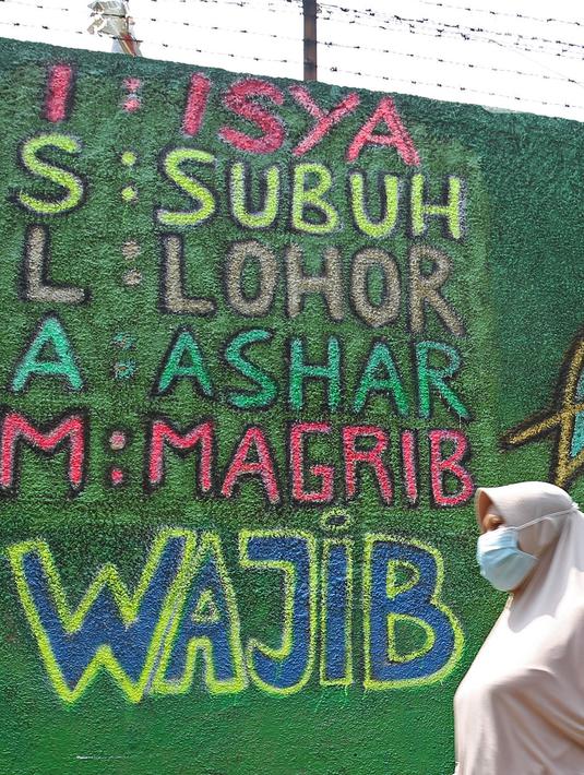 Warga berjalan di depan mural bernuansa Islami di Gang Pelangi, kawasan Kalibata, Jakarta, Jumat (23/4/2021). Mural bernuansa Islami tersebut dibuat untuk menghiasi dan meramaikan pintu masuk gang sekaligus mengingatkan masyarakat untuk selalu beribadah dan bershalawat (Liputan6.com/Herman Zakharia)