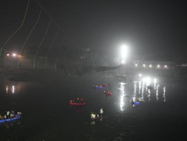 Tim penyelamat di kapal mencari di sungai Machchu di sebelah jembatan kabel yang runtuh di kota Morbi di negara bagian barat Gujarat, India, Senin, 31 Oktober 2022. Jembatan gantung kabel berusia seabad runtuh ke sungai Minggu malam, menyebabkan ratusan orang terjun. di dalam air, kata para pejabat. (AP/Ajit Solanki)