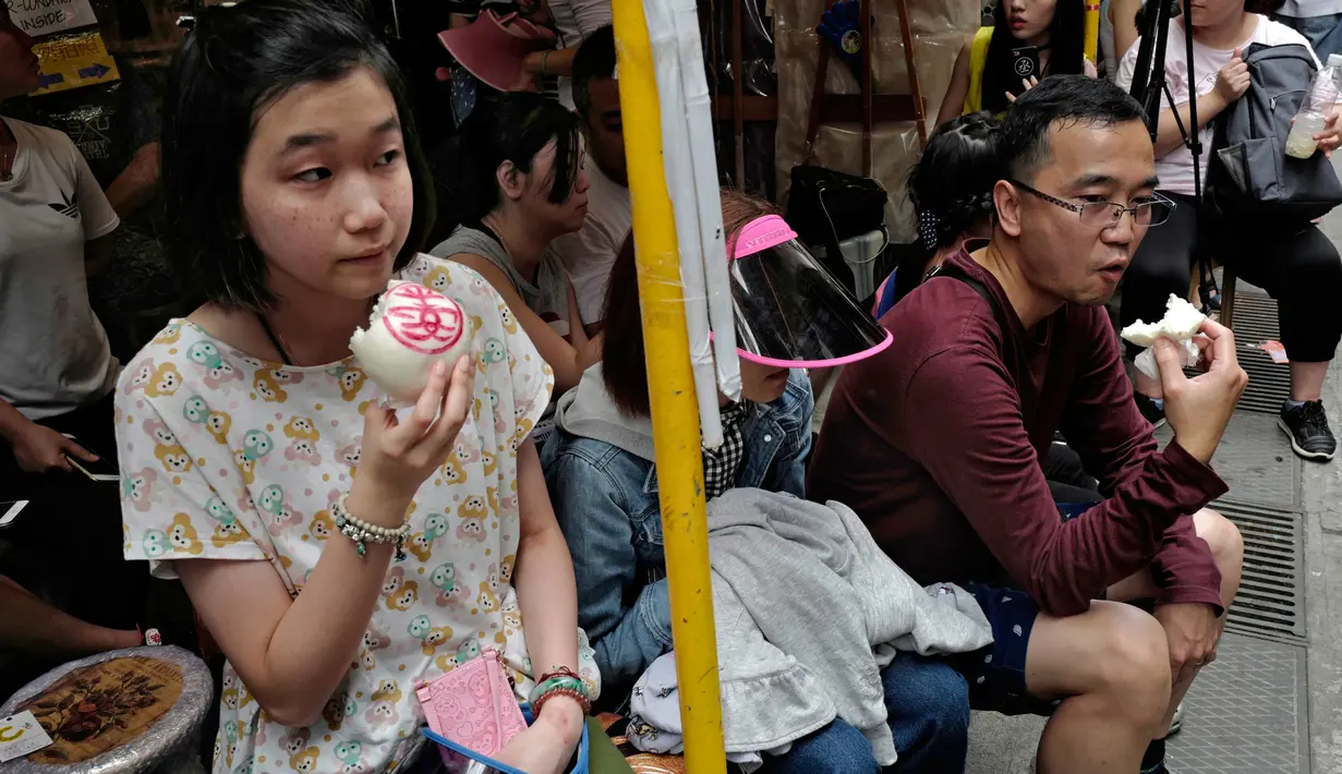 Sejumlah warga memakan roti atau bun saat perayaan Festival Cheung Chau Bun di Hong Kong (5/3). Festival ini diadakan di pulau kecil yang berada sekitar 10 kilometer dari Pulau Hong Kong yang bernama Pulau Cheung Chau. (AP Photo/Vincent Yu)