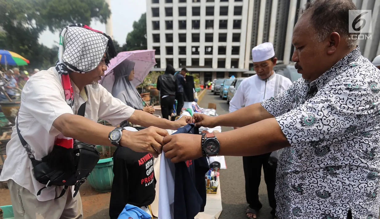 Calon pembeli melihat kaos #2019GantiPresiden di halaman Masjid Istiqlal, Jakarta, Jumat (10/8). Pedagang menjual kaos lengan panjang dan pendek berwarna putih, hitam, biru dan merah. (Liputan6.com/Fery Pradolo)