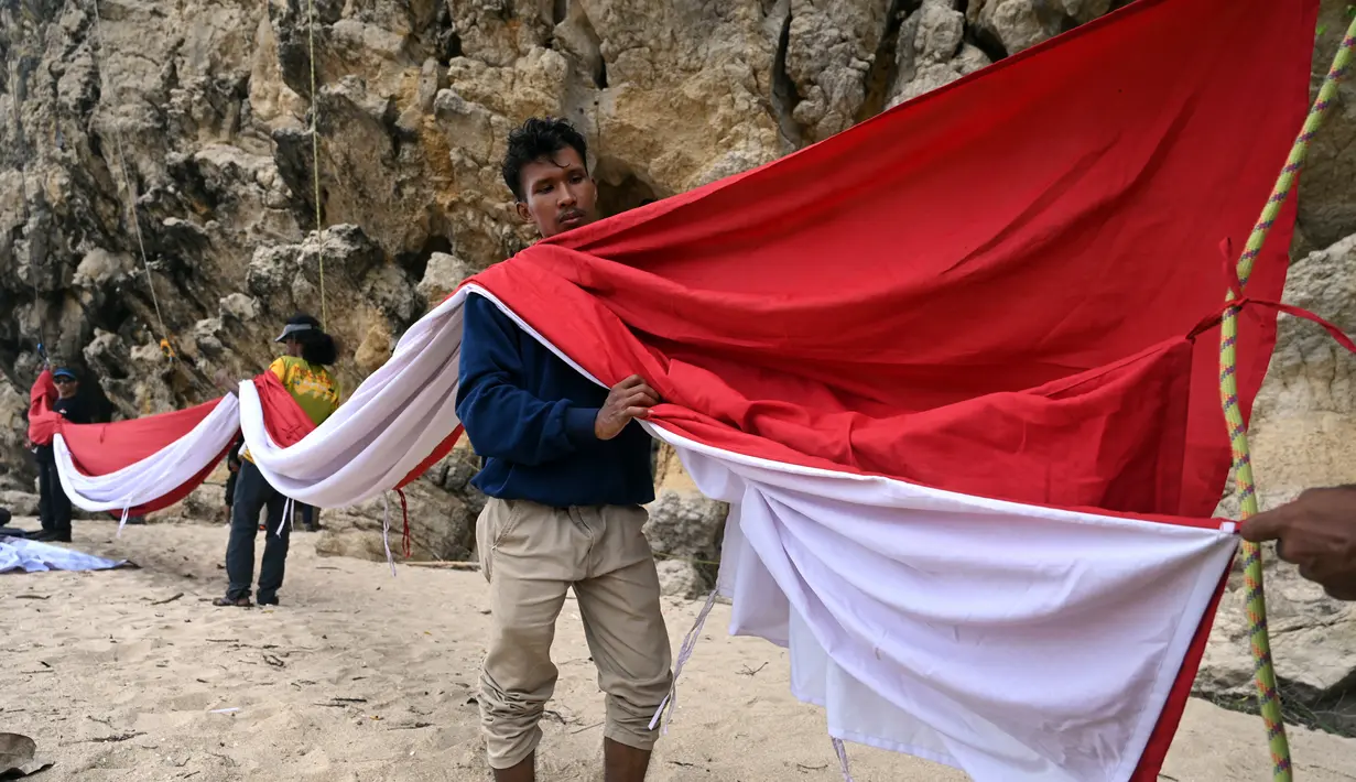 Sekelompok mahasiswa bersiap untuk mengibarkan bendera Merah Putih berukuran besar menjelang perayaan Hari Ulang Tahun ke-77 Republik Indonesia di Pantai Lhoknga, Aceh, 16 Agustus 2022. Pengibaran bendera Merah Putih berukuran besar yang dilakukan pada sebuah tebing ini untuk memeriahkan Hari Ulang Tahun ke-77 Republik Indonesia. (CHAIDEER MAHYUDDIN/AFP)