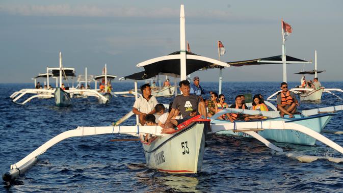 Wisatawan di atas perahu selama tamasya menyaksikan lumba-lumba di perairan Pantai Lovina di Singaraja, Bali, Jumat (30/10/2020). Pantai Lovina merupakan salah satu destinasi pariwisata di Bali yang sering dikunjungi untuk menikmati matahari terbit dan lumba-lumba di laut lepas (SONNY TUMBELAKA/AFP)