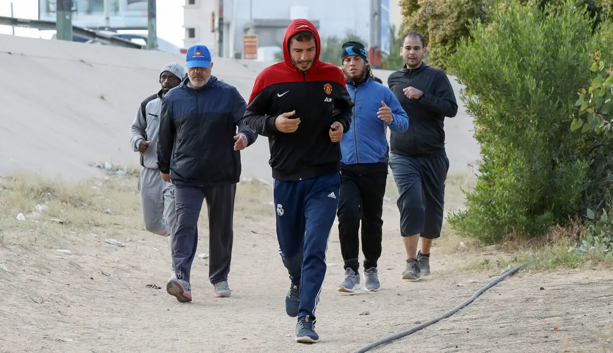 Para pria melakukan jogging sebelum bermain sepak bola di lapangan tanah sebelum buka puasa selama bulan Ramadhan, di ibu kota Libya, Tripoli (24/4/2021). (AFP/Mahmud Turkia)