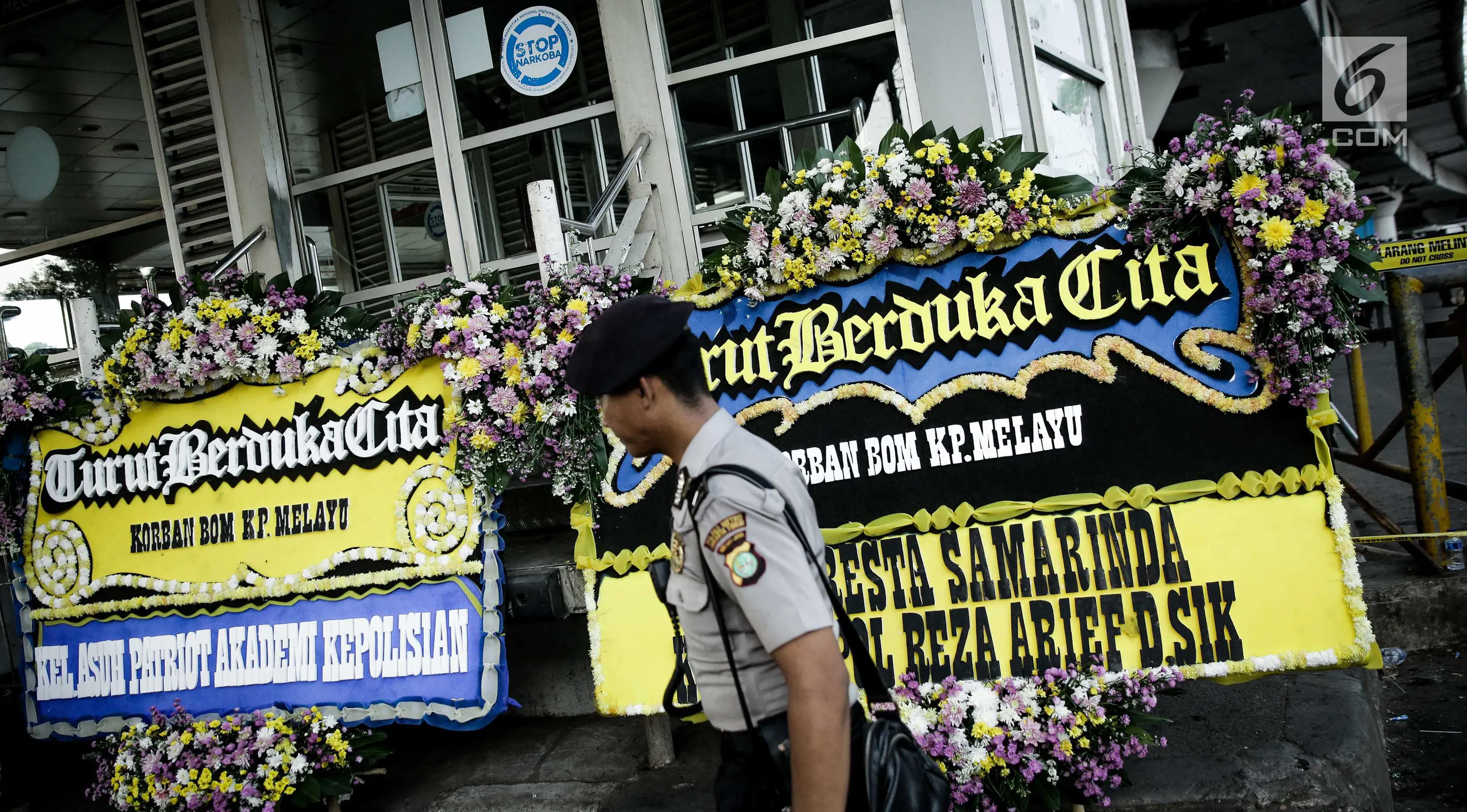 Anggota kepolisian melintas dekat karangan bunga di dekat lokasi ledakan bom, Terminal Kampung Melayu, Kamis (25/5). Karangan bunga itu tanda duka cita pihak kepolisian terhadap tiga polisi yang gugur dan para korban luka. (Liputan6.com/Faizal Fanani)