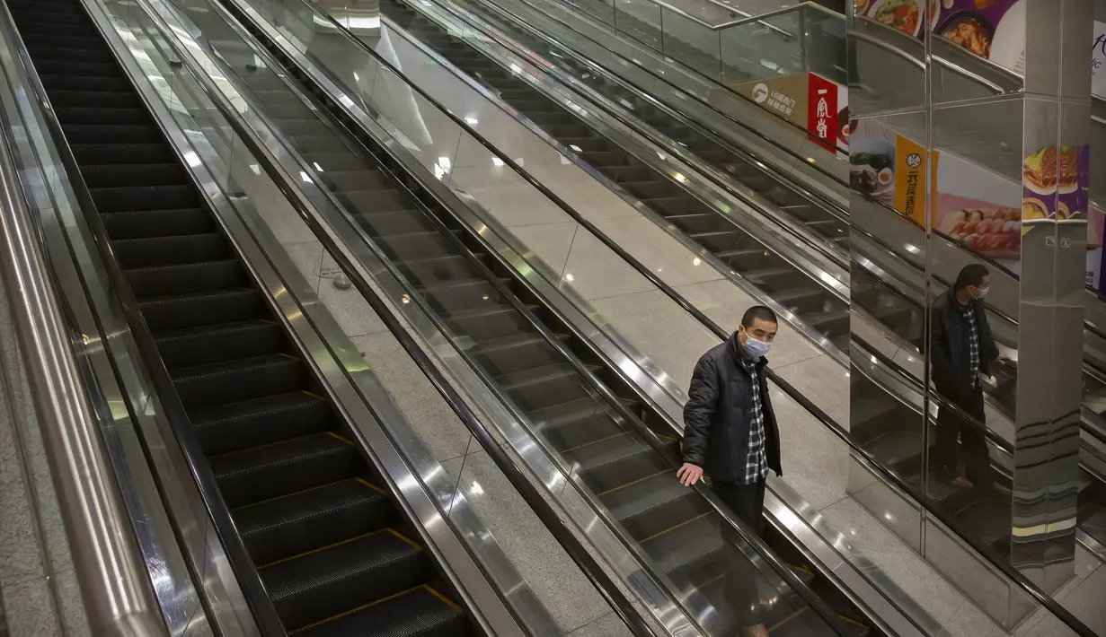 Seorang pria mengenakan masker turun menggunkan eskalator di pusat perbelanjaan yang sepi pengunjung di Beijing (28/1/2020).  Mewabahnya virus corona membuat pusat perbelanjaan di Beijing, China, sepi pengunjung. (AP Photo/Mark Schiefelbein)