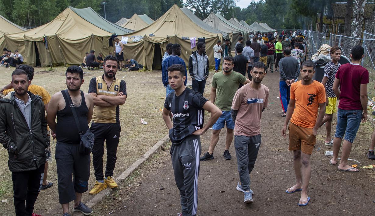 Para migran berjalan di dalam kamp pengungsi yang baru dibangun di tempat latihan militer Rudninkai, sekitar 38km (23,6 mil) selatan dari Vilnius, Lituania, Rabu (4/8/2021). (AP Photo/Mindaugas Kulbis)