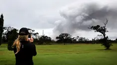 Marie Brant, dari California, mengambil gambar asap tebal yang berembus dari puncak gunung berapi Kilauea di Hawaii. Kamis (17/5). Para wisatawan tetap santai dan justru menjadikan letusan gunung ini sebagai objek wisata. (AP Photo/Caleb Jones)