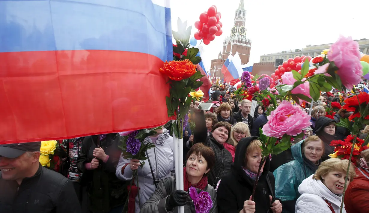 Puluhan orang berjalan sambil membawa bendera dan bunga plastik saat peringatan Hari Buruh Internasional (May Day) di Red Square, Moskow, Jumat (1/5/2015). (REUTERS/Maxim Zmeyev)