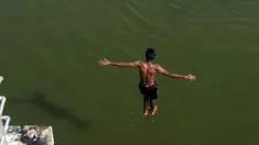 Seorang pemuda India melompat ke dalam sungai yang tercemar di pinggiran Chennai, India, Rabu (5/4). Sejumlah warga di India biasa mandi di sungai saat cuaca panas. (AFP PHOTO / ARUN SANKAR)
