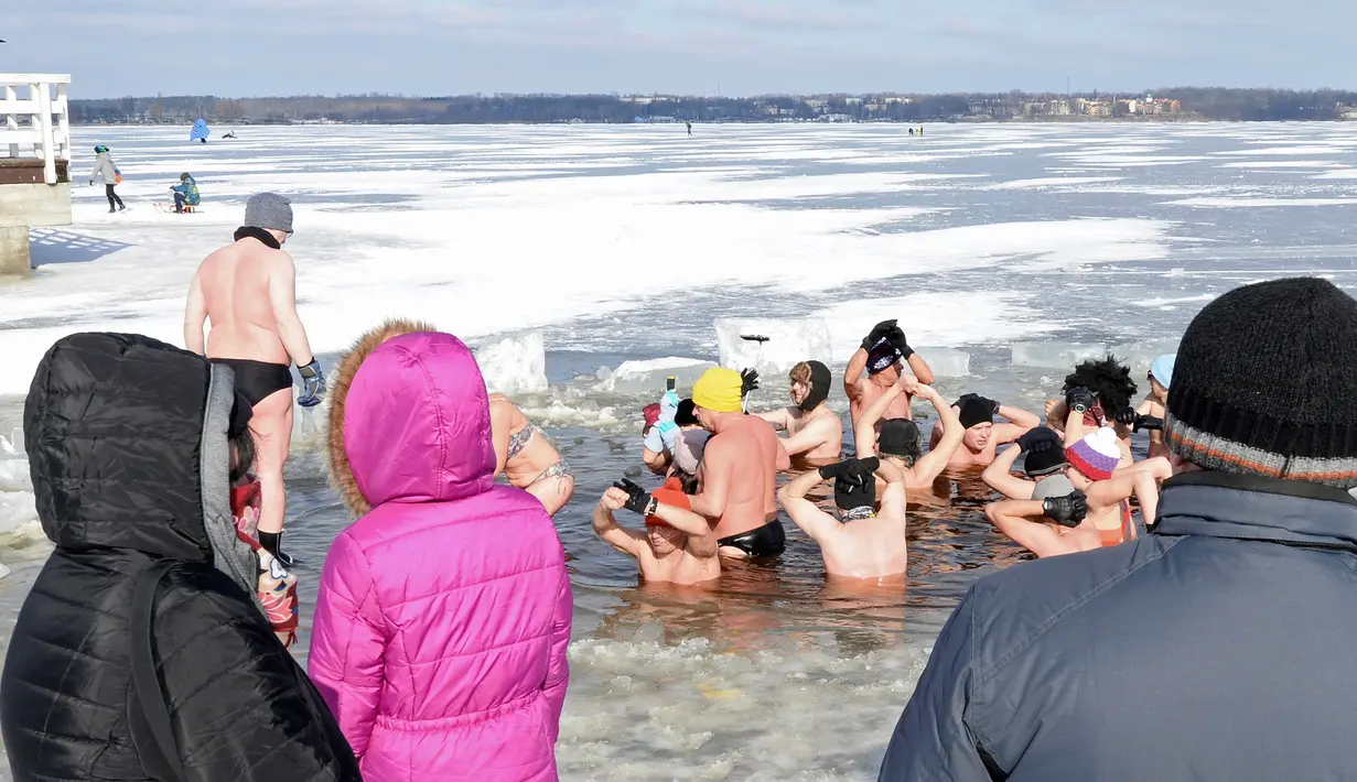 Orang-orang menyaksikan penggemar renang es di Danau Zalew Zegrzynski di Nieporet, Polandia, Minggu (25/2). Gelombang dingin sedang melanda Polandia. (AP Photo/Alik Keplicz)