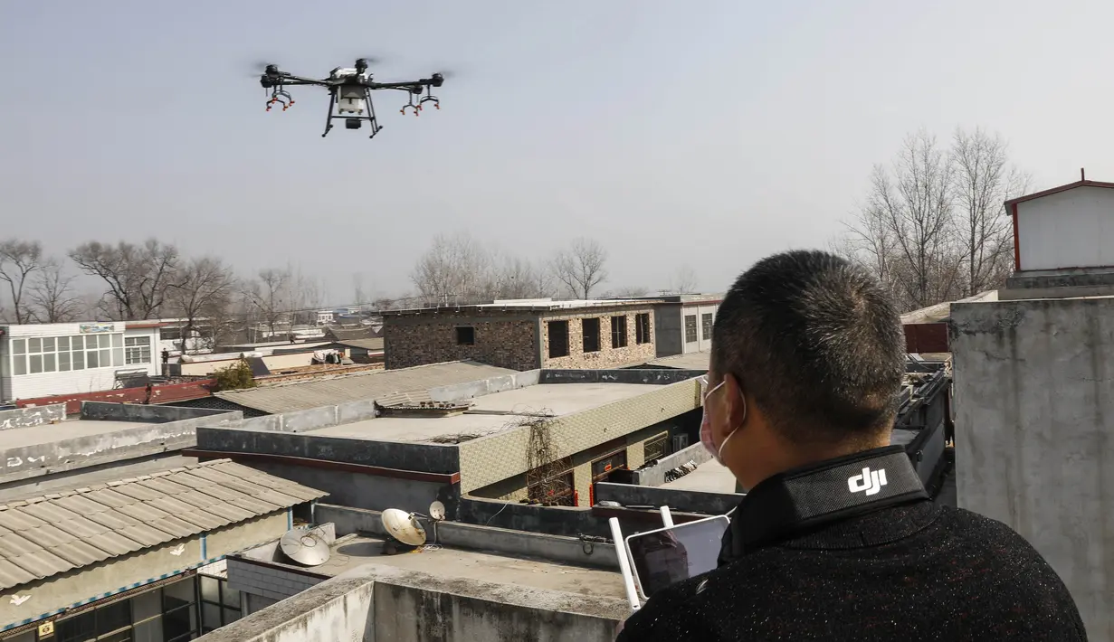 Seorang warga mengoperasikan drone yang membawa cairan desinfektan yang akan disemprotkan ke sebuah desa di Pingdingshan, Provinsi Henan, China (31/1/2020).  Cara ini digunakan untuk mencegah sekaligus mematikan partikel-partikel virus corona yang menyebar di setiap sudut daerah. (AFP Photo/Str)
