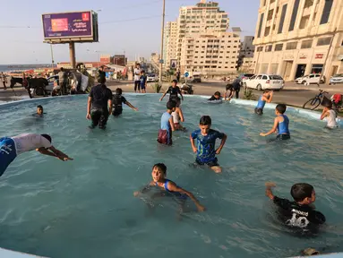 Anak-anak Palestina bermain di air mancur umum selama hari musim panas di Kota Gaza (20/7/2020). Musim panas yang terjadi di Palestina membuat anak-anak memenuhi air mancur. Mereka berupaya mendinginkan tubuh mereka dengan cara berenang di air mancur tersebut. (AFP Photo/Mahmud Hams)