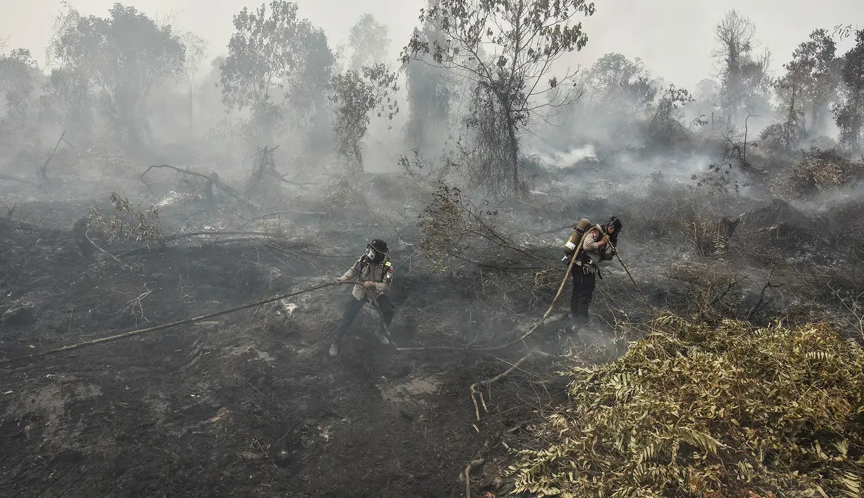 Polisi yang mengenakan perlengkapan pemadam kebakaran memadamkan kebakaran lahan gambut di Tambang, Kabupaten Kampar, Provinsi Riau, Selasa,  25 Agustus 2026. (AFP/ Wahyudi)