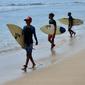 Anak-anak berjalan dengan papan selancar mereka di pantai Kuta di pulau resor Bali (4/10/2021). Pemerintah melonggarkan secara bertahap PPKM berjenjang dengan membuka Bandara Internasional Ngurah Rai untuk kedatangan internasional mulai 14 Oktober. (AFP/Sony Tumbelaka)