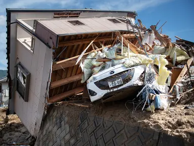 Sebuah mobil tertimpa rumah yang rusak usai banjir melanda Kumano, Prefektur Hiroshima, Jepang, Senin (9/7). Sebanyak 75 orang tewas dalam bencana tersebut. (Martin BUREAU/AFP)