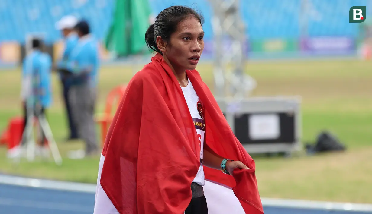 Pelari putri Indonesia, Odekta Elvina Naibaho membawa bendera Merah Putih setelah menyelesaikan nomor lari 10.000 meter SEA Games 2023 di Stadion Morodok Techo National Stadium, Phnom Penh, Kamboja, Jumat (12/5/2023). Odekta meraih medali perunggu dengan catatan waktu 35 menit 31,03 detik sementara medali emas dan perak direbut dua atlet Vietnam, Thi Oanh Nguyen (35 menit 11,53 detik) dan Thi Hong Le Pham (35 menit 21,09 detik). (Bola.com/Abdul Aziz)