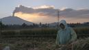 Seorang petani bekerja dengan latar belakang Gunung Raung mengeluarkan awan panas di Kabupaten Jember, Jawa Timur, Minggu (12/7/2015). (AFP PHOTO)