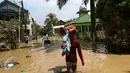 Seorang pedagang melewati banjir sambil membawa dagangannya di kompleks Pondok Gede Permai, Jatiasih, Bekasi, Jumat (22/4). Pedagang berjualan alat kebersihan untuk membersihkan sisa lumpur yang terbawa banjir di kawasan itu. (Liputan6.com/Fery Pradolo)