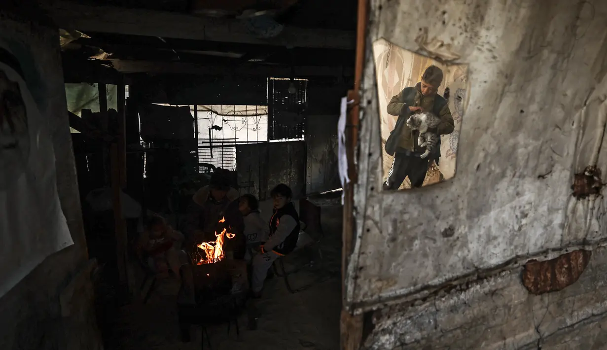 Sebuah keluarga Palestina menghangatkan diri di sebelah api pada hari hujan di Khan Yunis, di Jalur Gaza selatan pada 19 Januari 2022. (Mahmud HAMS / AFP)