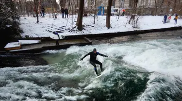 Seorang pria menaklukkan ombak saat berselancar di Sungai Eisbach selama hari musim dingin di Munich, Jerman, 4 Januari 2017. Eisbach merupakan sungai buatan dengan panjang dua kilometer dan arusnya pun merupakan buatan. (Mark RALSTON/AFP)